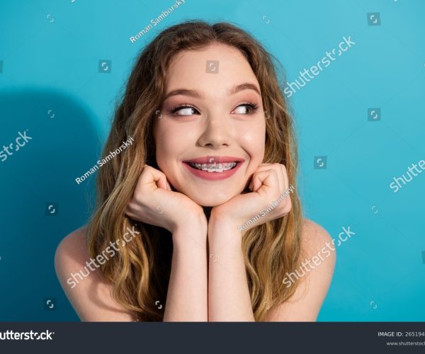 stock-photo-smiling-pretty-young-woman-with-braces-resting-hands-on-face-against-vibrant-blue-background-2651944947